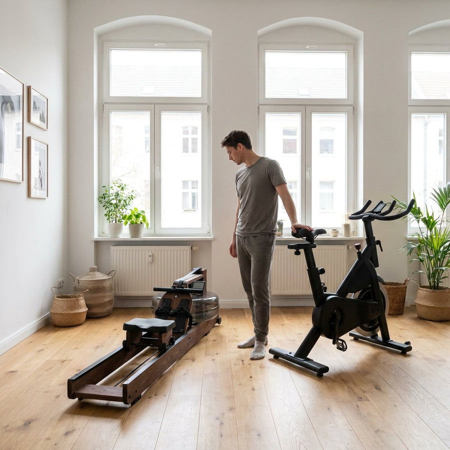 Moderne thuisgym met roeitrainer en hometrainer naast elkaar, terwijl een sporter twijfelend kiest in zacht daglicht.